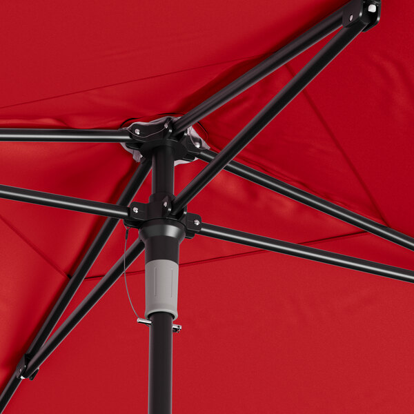 A close up of a red Lancaster Table & Seating umbrella with black poles.