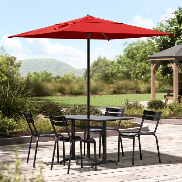 A black table and chairs under a red Lancaster Table & Seating umbrella.