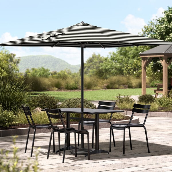 A black and white striped Lancaster Table & Seating umbrella covering a table with chairs on an outdoor patio.