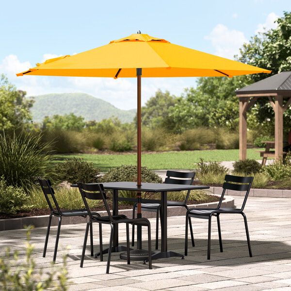 A Lancaster Table & Seating yellow woodgrain umbrella on a patio table with chairs.