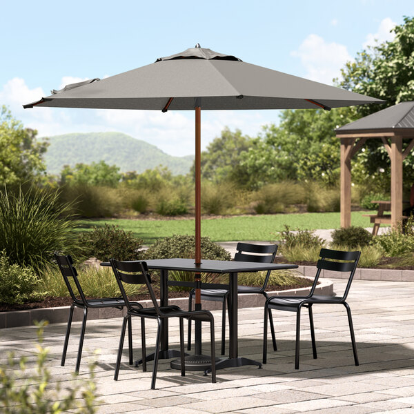 A Lancaster Table & Seating woodgrain umbrella over a table with chairs on a patio.