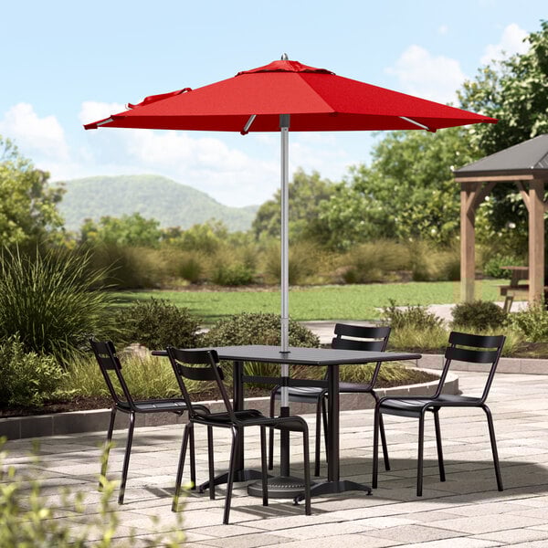 A Lancaster Table & Seating round table and chairs with a red umbrella.