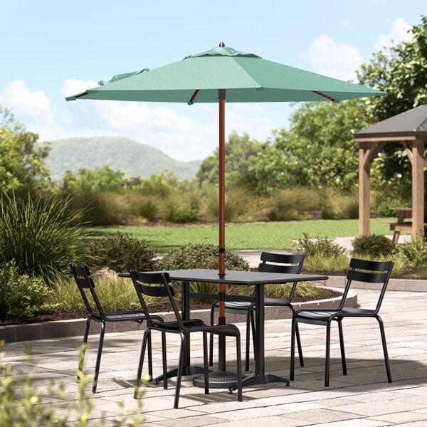 A Lancaster Table & Seating woodgrain aluminum umbrella over a table with chairs on a stone patio.