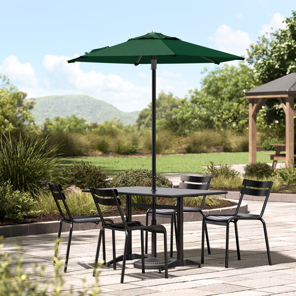 A forest green Lancaster Table & Seating umbrella shading a black table and chairs on an outdoor patio.