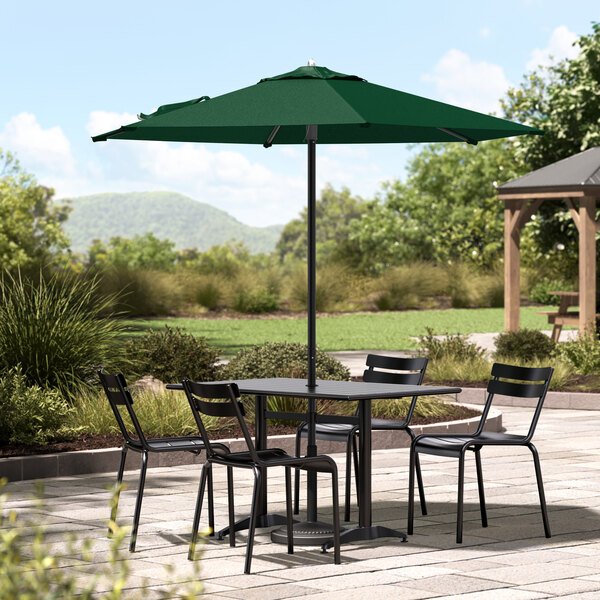 A Lancaster Table & Seating forest green umbrella over a table with chairs on a stone patio.