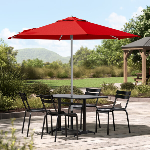 A table with four black chairs and a red Lancaster Table & Seating umbrella.