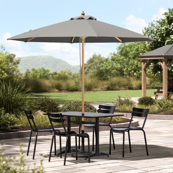 A table with chairs under a Lancaster Table & Seating pewter gray umbrella on a patio.