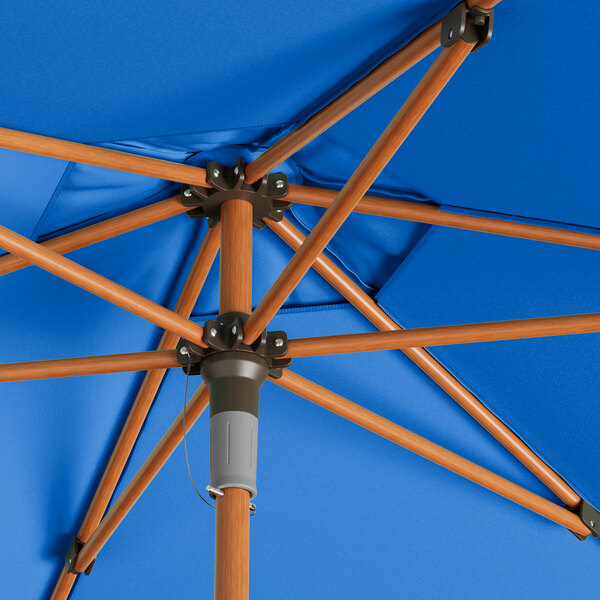 A Lancaster Table & Seating cobalt blue umbrella with woodgrain pole.