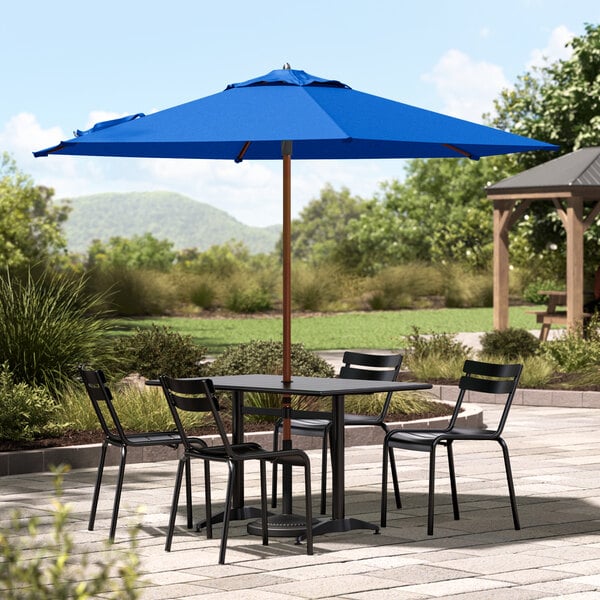 A wooden table with black chairs under a blue Lancaster Table & Seating umbrella.