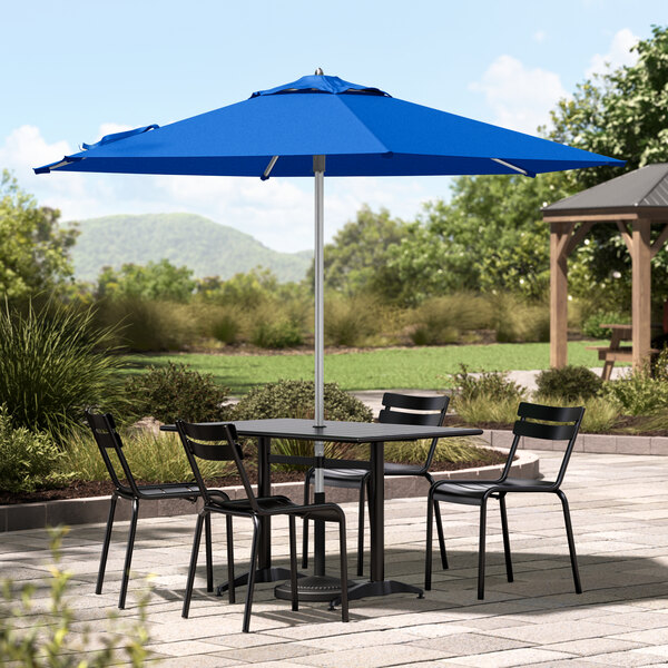 A table and chairs under a blue Lancaster Table & Seating umbrella on a patio.