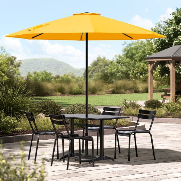 A Lancaster Table & Seating round yellow umbrella on a patio table with chairs.