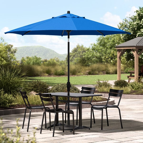 A black table with chairs under a blue Lancaster Table & Seating umbrella.