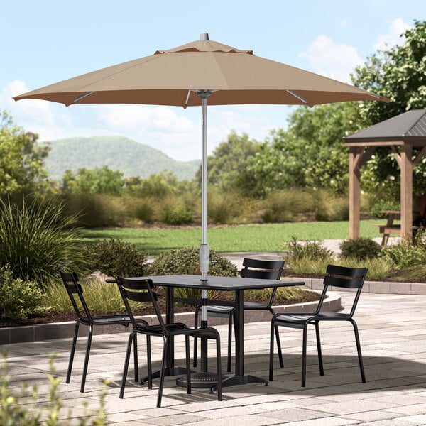 A Lancaster Table & Seating round silver umbrella over a table with chairs on a stone patio.