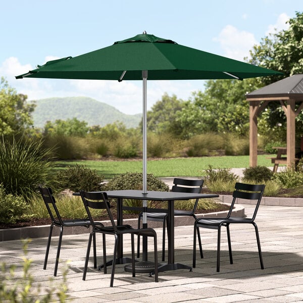 A Lancaster Table & Seating forest green umbrella on a patio table with chairs.