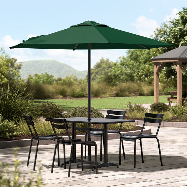 A Lancaster Table & Seating forest green umbrella over a table with chairs on an outdoor patio.