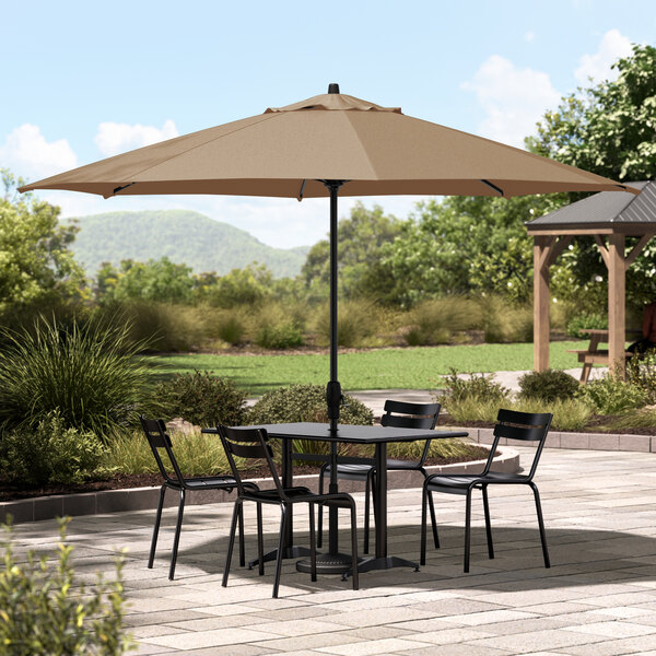 A table and chairs under a Lancaster Table & Seating black aluminum umbrella on a patio.