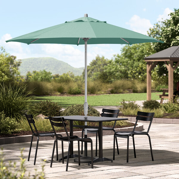 A table and chairs under a silver Lancaster Table & Seating umbrella on a patio.