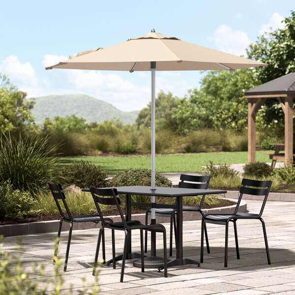 A Lancaster Table & Seating sand umbrella shading a table and chairs on a stone patio.