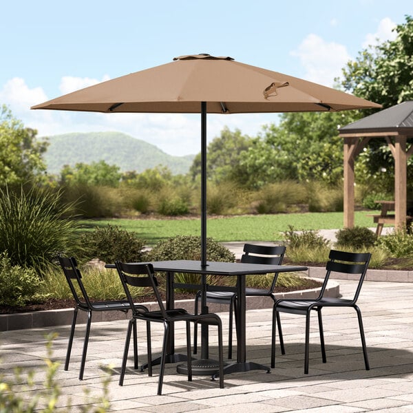 A table and chairs under a Lancaster Table & Seating mocha umbrella on a stone patio.