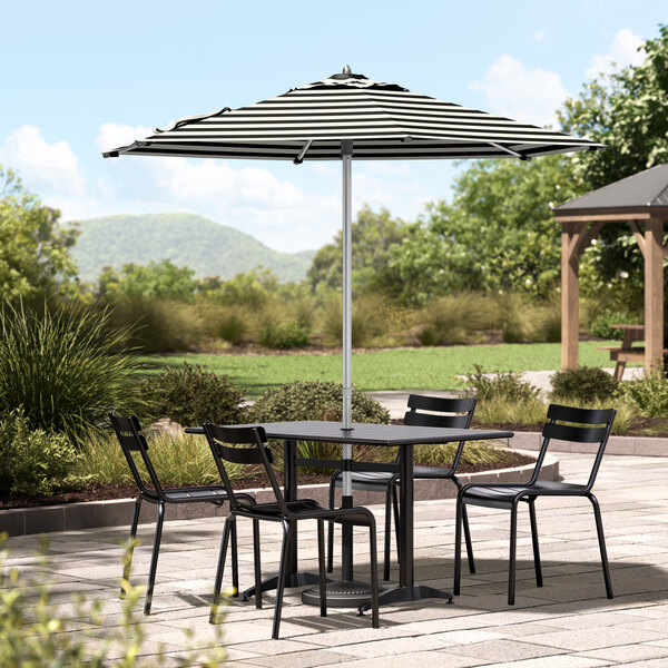 A Lancaster Table & Seating black and white striped umbrella over a table and chairs on a stone patio.