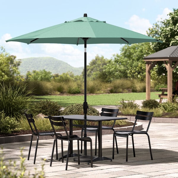 A table and chairs under a black umbrella on an outdoor patio.