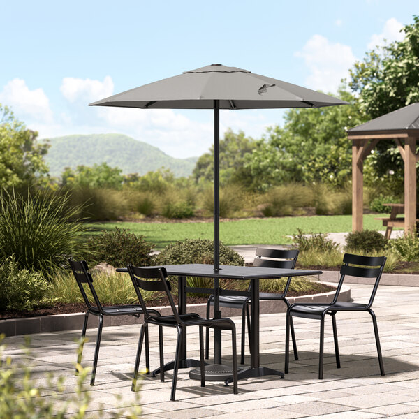 A black Lancaster Table & Seating table and chairs on a stone patio under a pewter gray umbrella.