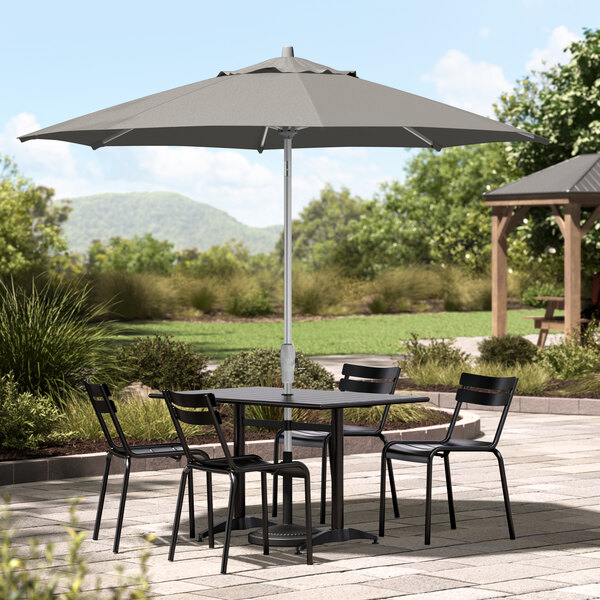 A Lancaster Table & Seating umbrella over a table and chairs on a patio.