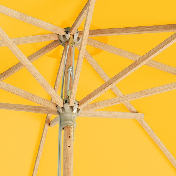 A Lancaster Table & Seating round bamboo umbrella with a yellow canopy and wooden poles.