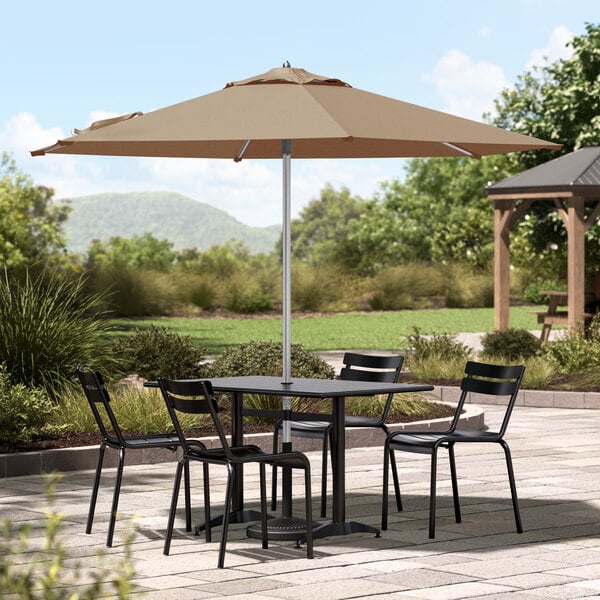 A round table and chairs under a tan Lancaster Table & Seating umbrella on a patio.