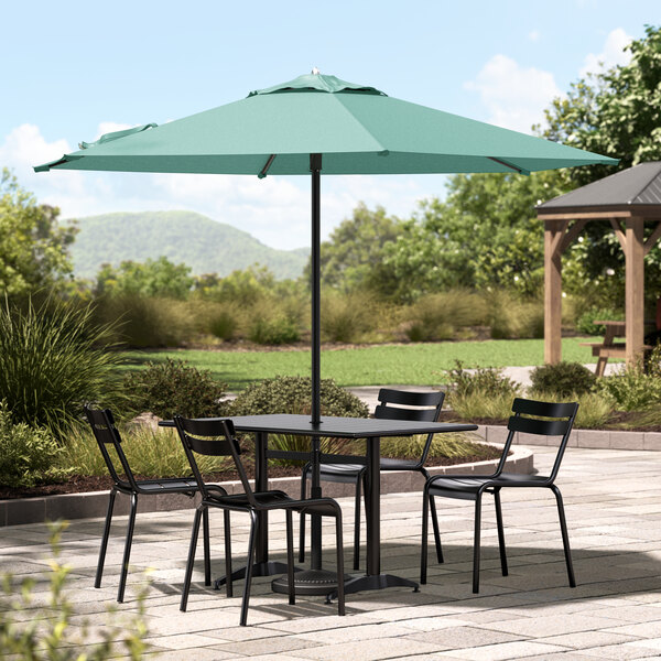 A black Lancaster Table & Seating umbrella shading a table and chairs on an outdoor patio.