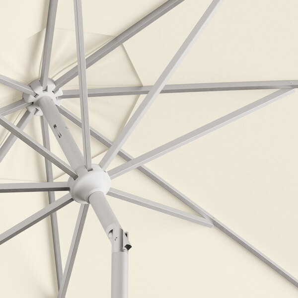A close up of a Lancaster Table & Seating ivory umbrella with a silver metal pole.