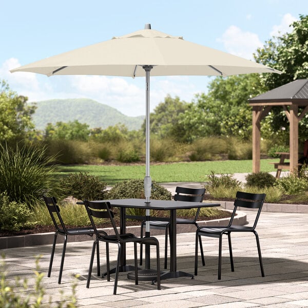 A table and chairs under a Lancaster Table & Seating ivory umbrella on a patio.