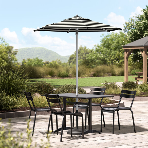 A black and white striped umbrella on a table with black chairs on a stone patio.