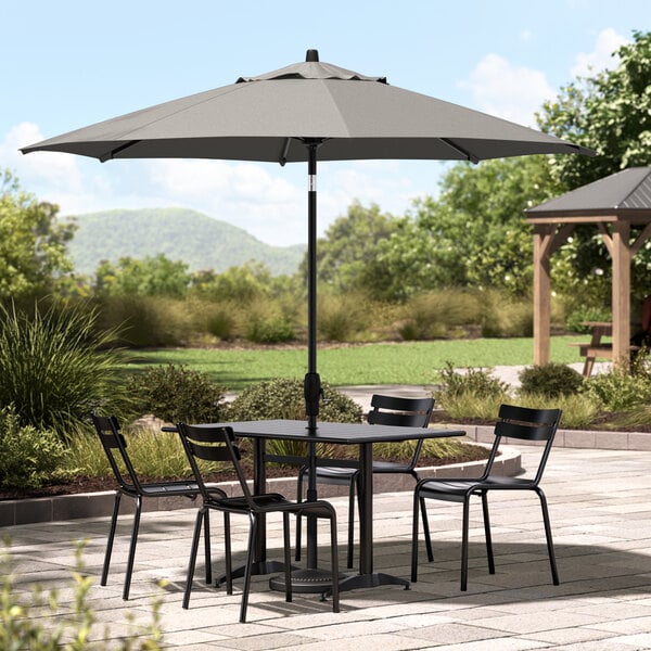 A black Lancaster Table & Seating umbrella over a table and chairs on a patio.