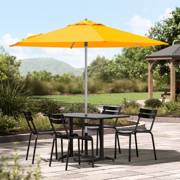 A Lancaster Table & Seating yellow umbrella on a patio table with chairs.