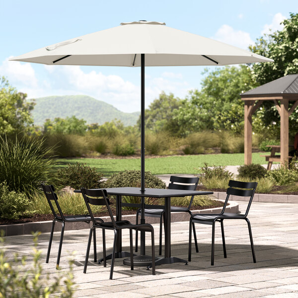 A Lancaster Table & Seating white umbrella over a table and chairs on a stone patio.