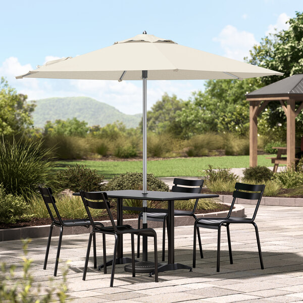 A Lancaster Table & Seating ivory umbrella over a table and chairs on an outdoor patio.