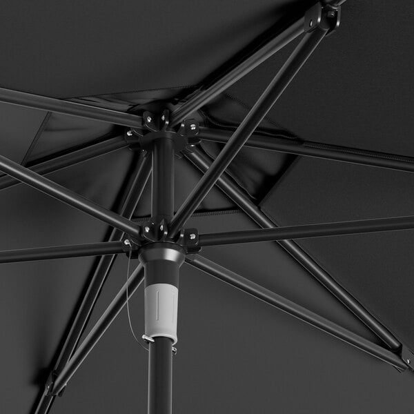 A Lancaster Table & Seating black umbrella with a black metal pole on a table in an outdoor patio.