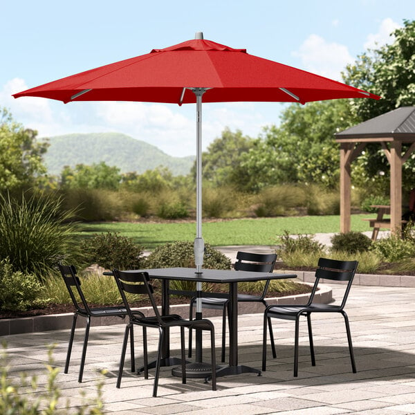 A table and chairs under a red Lancaster Table & Seating umbrella.