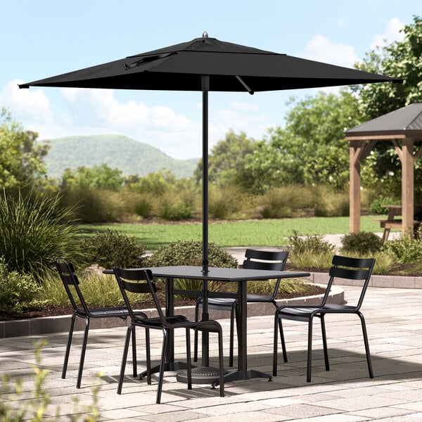 A Lancaster Table & Seating black umbrella over a table with chairs on a patio.