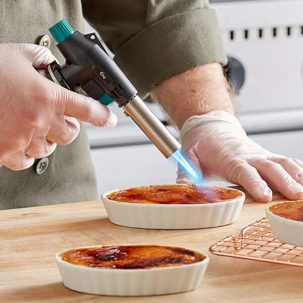 A person using a Choice adjustable butane torch to cook a dessert on a white dish.