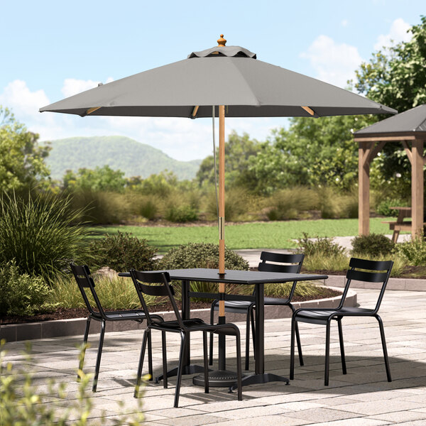 A Lancaster Table & Seating round pewter gray umbrella over a table with chairs on a stone patio.