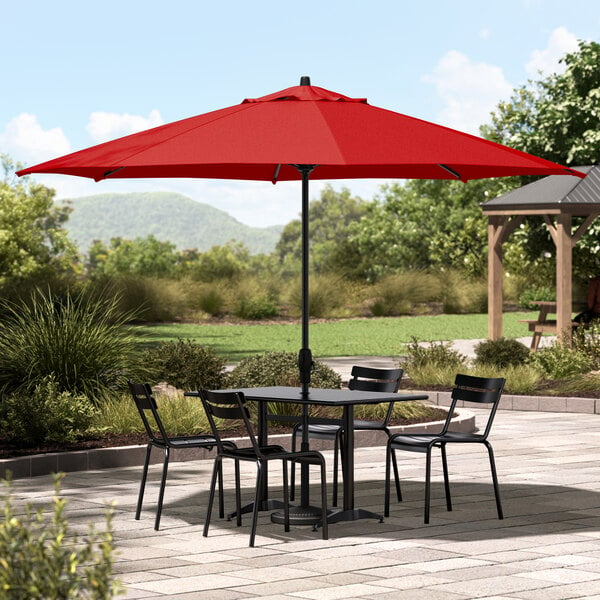 A Lancaster Table & Seating black aluminum table and chairs under a red umbrella on a patio.