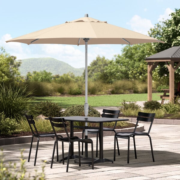 A table with chairs under a Lancaster Table & Seating round sand umbrella on a patio.