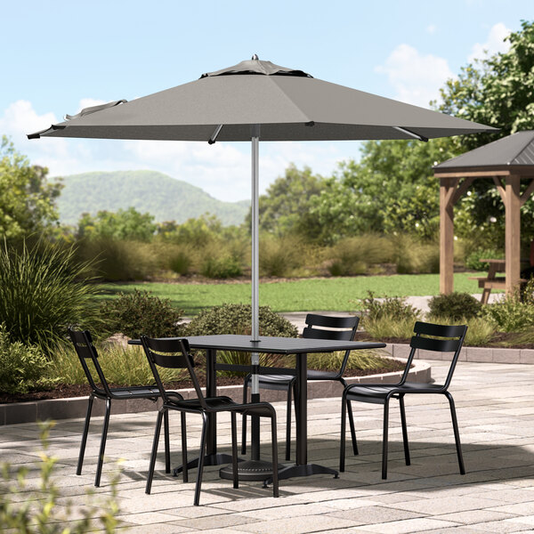A Lancaster Table & Seating graphite umbrella over a table and chairs on a patio.
