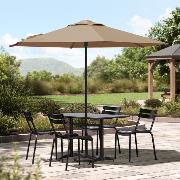 A black Lancaster Table & Seating umbrella over a table and chairs on an outdoor patio.