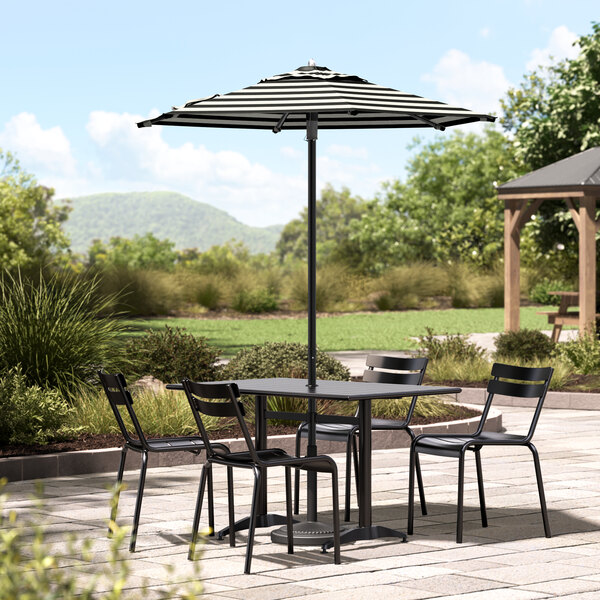 A table and chairs under a Lancaster Table & Seating black and white striped umbrella on a patio.