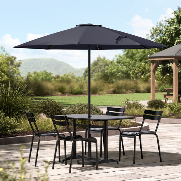 A table and chairs under a Lancaster Table & Seating indigo blue umbrella on a stone patio.