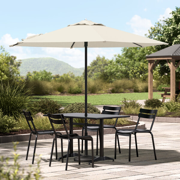 A table and chairs under a Lancaster Table & Seating ivory umbrella on a patio.