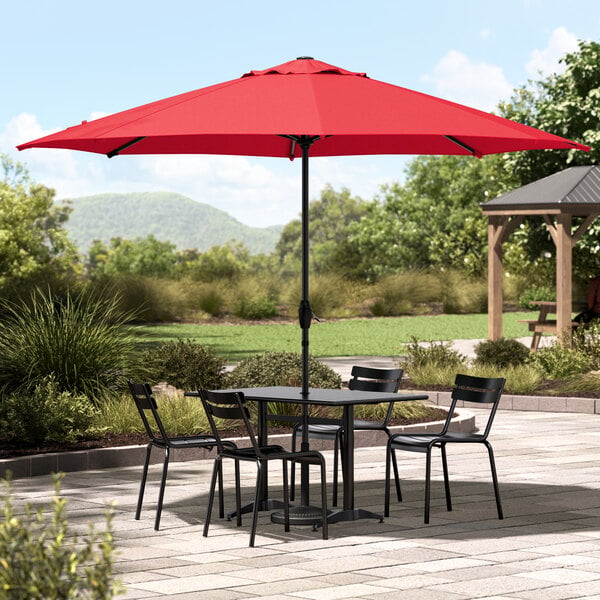 A table and chairs under a red Lancaster Table & Seating umbrella on a patio.